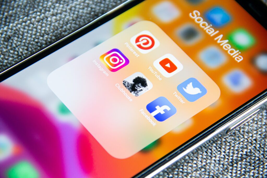 A smartphone screen displaying a folder labeled Social Media, containing icons for Pinterest, Instagram, YouTube, Clubhouse, Twitter, and Facebook. The background is a colorful, blurred gradient.